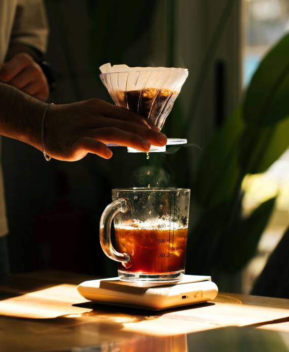 A person expertly pours hot water over coffee grounds in a Chemex, demonstrating the precision of pour-over brewing to extract nuanced flavours—key to tasting specialty coffee like a pro at Roasters Co.
